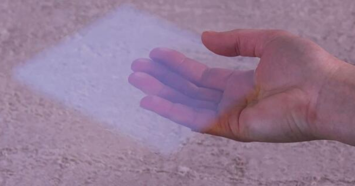 Una mano que sostiene un trozo cuadrado de monolito de aerogel a través del cual se pueden ver los dedos del sujeto.